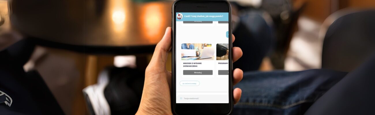 Osoba trzymająca w ręku telefon komórkowy z otwartym okienkiem chatbota ze strony dlanaswjm.pl.