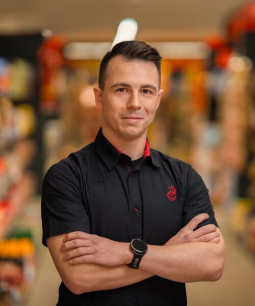 Mężczyzna w stroju służbowym na tle sklepu Biedronka.