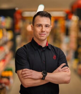 Mężczyzna w stroju służbowym na tle sklepu Biedronka.