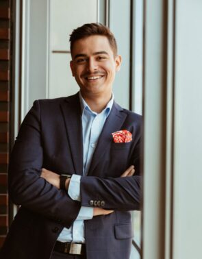 Мужчына ў куртцы і кашулі ўсміхаецца ў камеру.